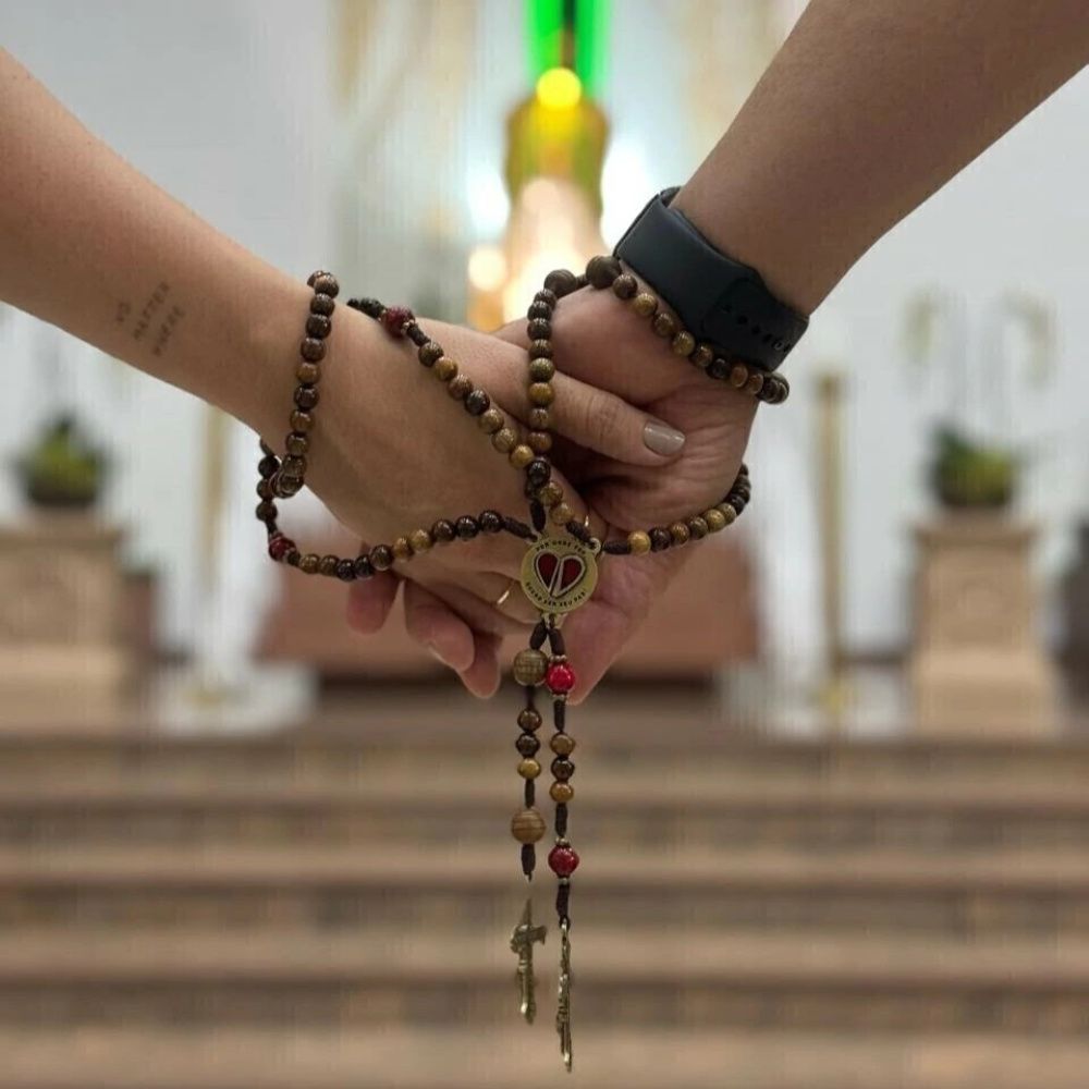 Casal de mãos dadas segurando o Terço dentro da igreja